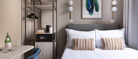 A hotel room with a bed, a desk, a chair, a wardrobe, and a painting on the wall.