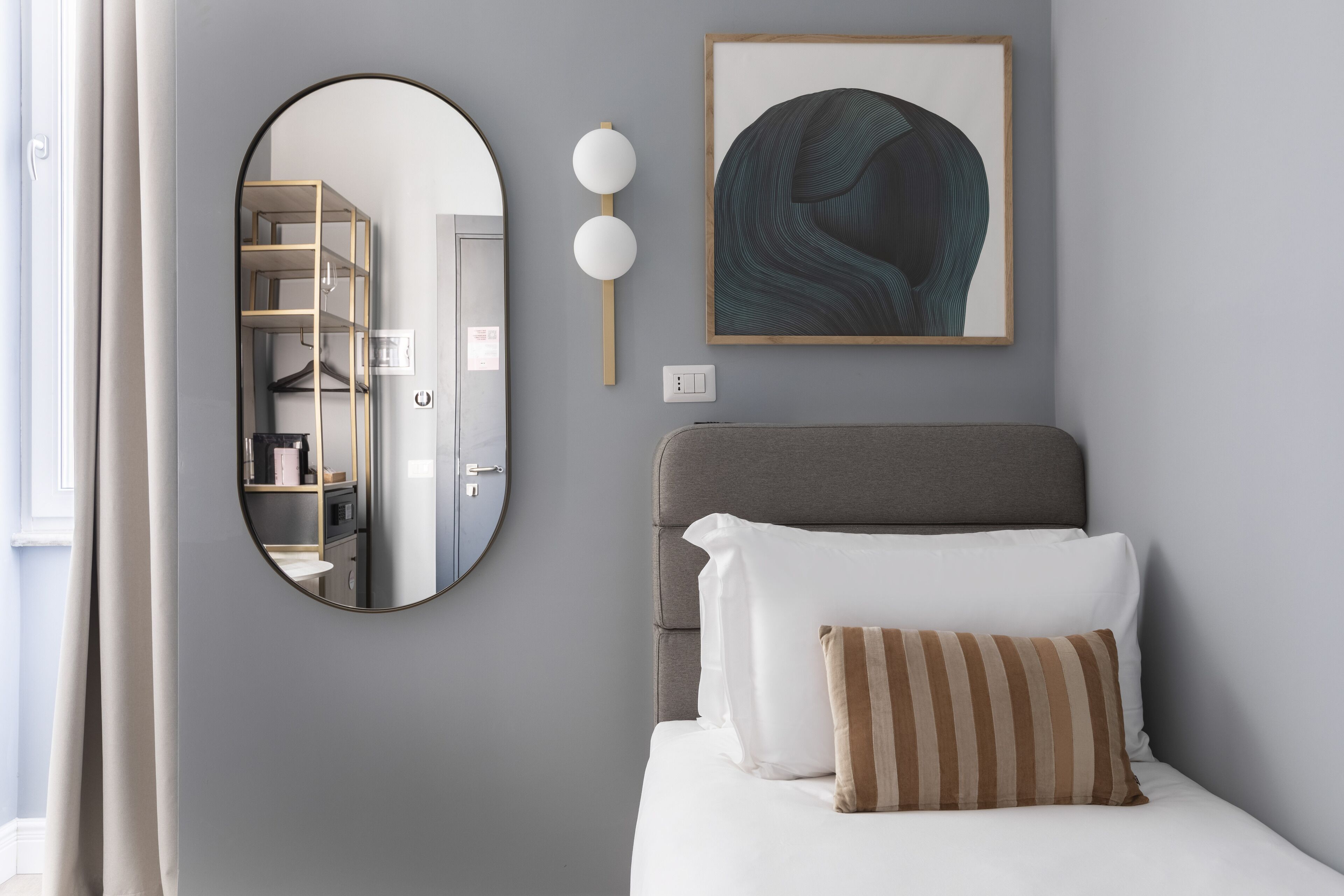 A bedroom with a bed, a mirror, a framed artwork, and a shelf with books.