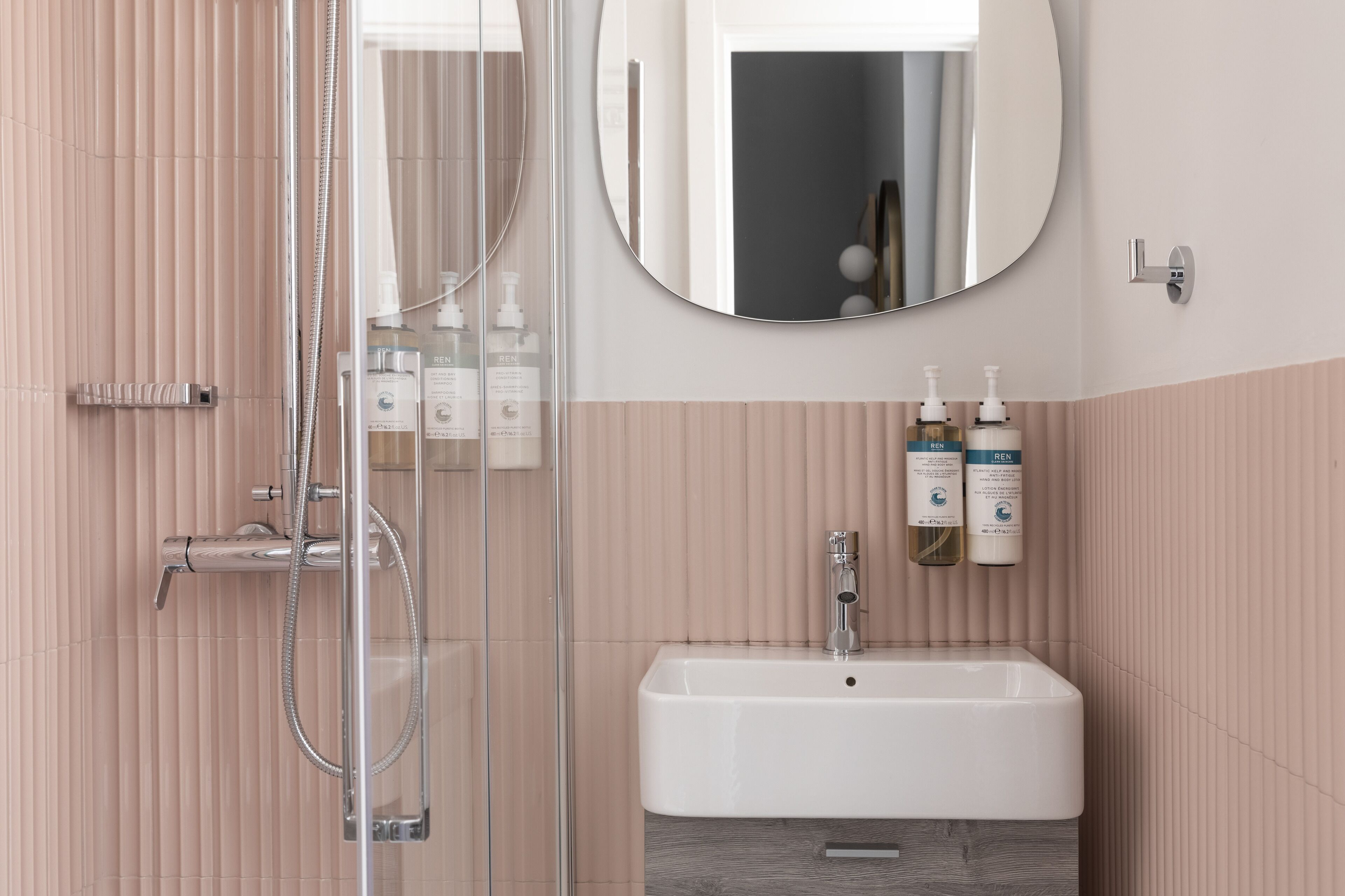 A modern bathroom with a glass shower enclosure, a white sink, and a round mirror.