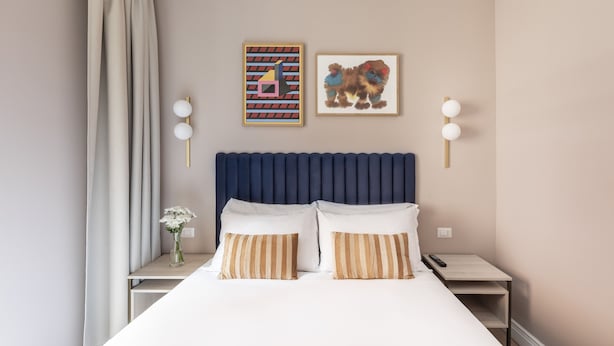 Una cama bien hecha con almohadones a rayas, un cabecero azul y dos lámparas fijadas a la pared.
