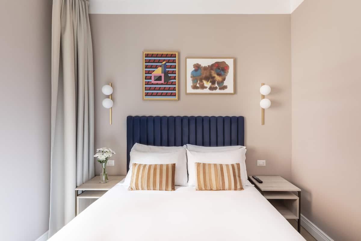 A neatly made bed with striped pillows, a blue headboard, and two wall-mounted lamps.