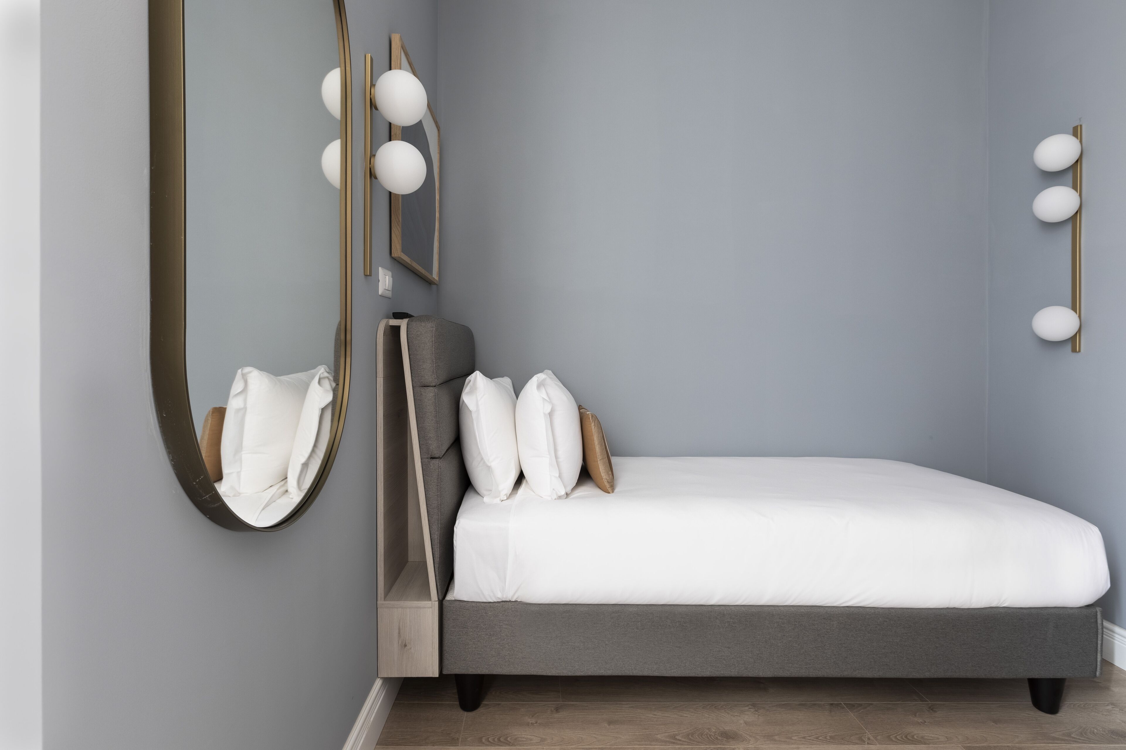 A bedroom with a bed, a mirror, and wall-mounted lighting.