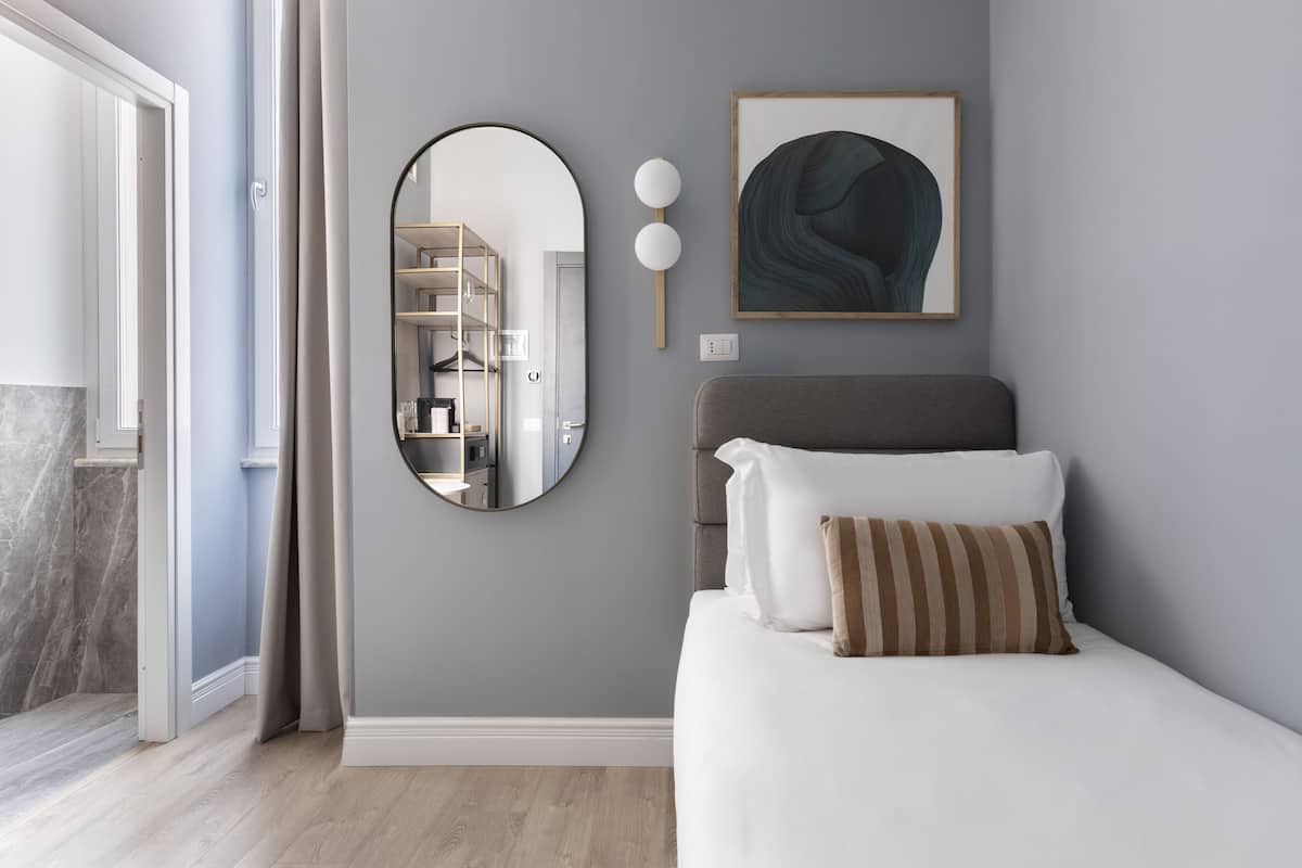 A bedroom with a bed, a round mirror, a framed abstract painting, and a wardrobe with a mirror.