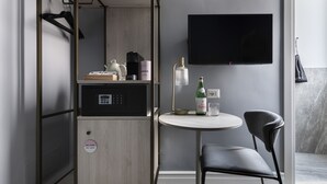 Habitación compacta con kitchenette, una mesa redonda con una silla, televisor montado en la pared y perchero.