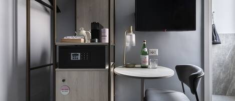 Habitación compacta con kitchenette, una mesa redonda con una silla, televisor montado en la pared y perchero.