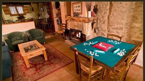 A cozy living room with a fireplace, a green sofa, a wooden coffee table, and a dining table set for a game. - Casa Rural Las Trojes (Tamajon)