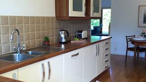A kitchen with wooden cabinets, a stainless steel sink, and a tiled backsplash. - The Eco-Flat (Sherborne)