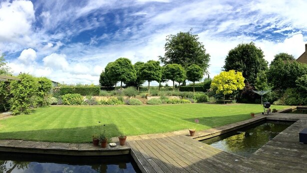 A well-maintained garden with a lawn, a wooden deck, and a small pond. - The Eco-Flat (Sherborne)