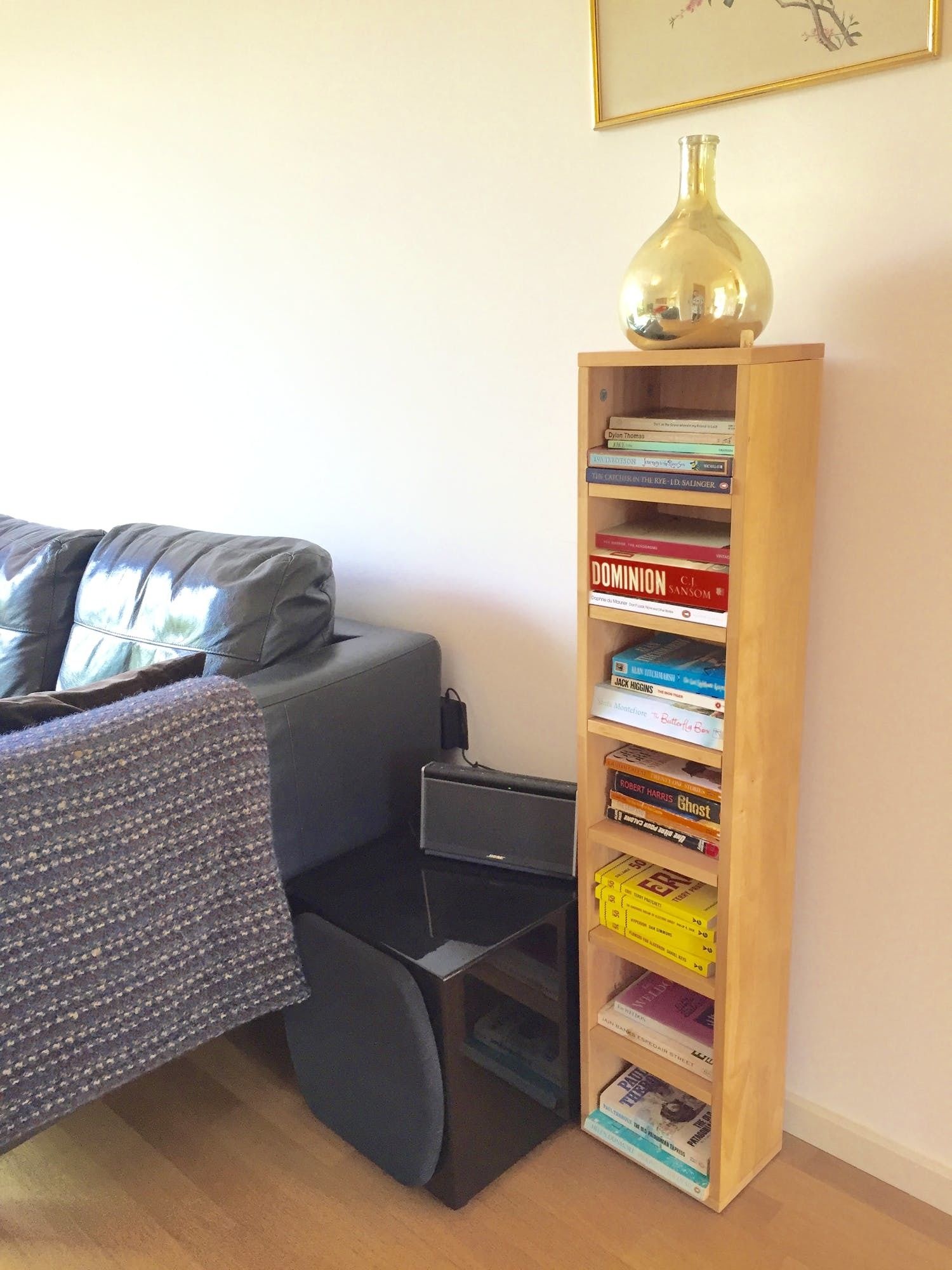 Une pièce avec un canapé gris, une bibliothèque en bois remplie de livres, une petite table avec une lampe et un tableau encadré accroché au mur.