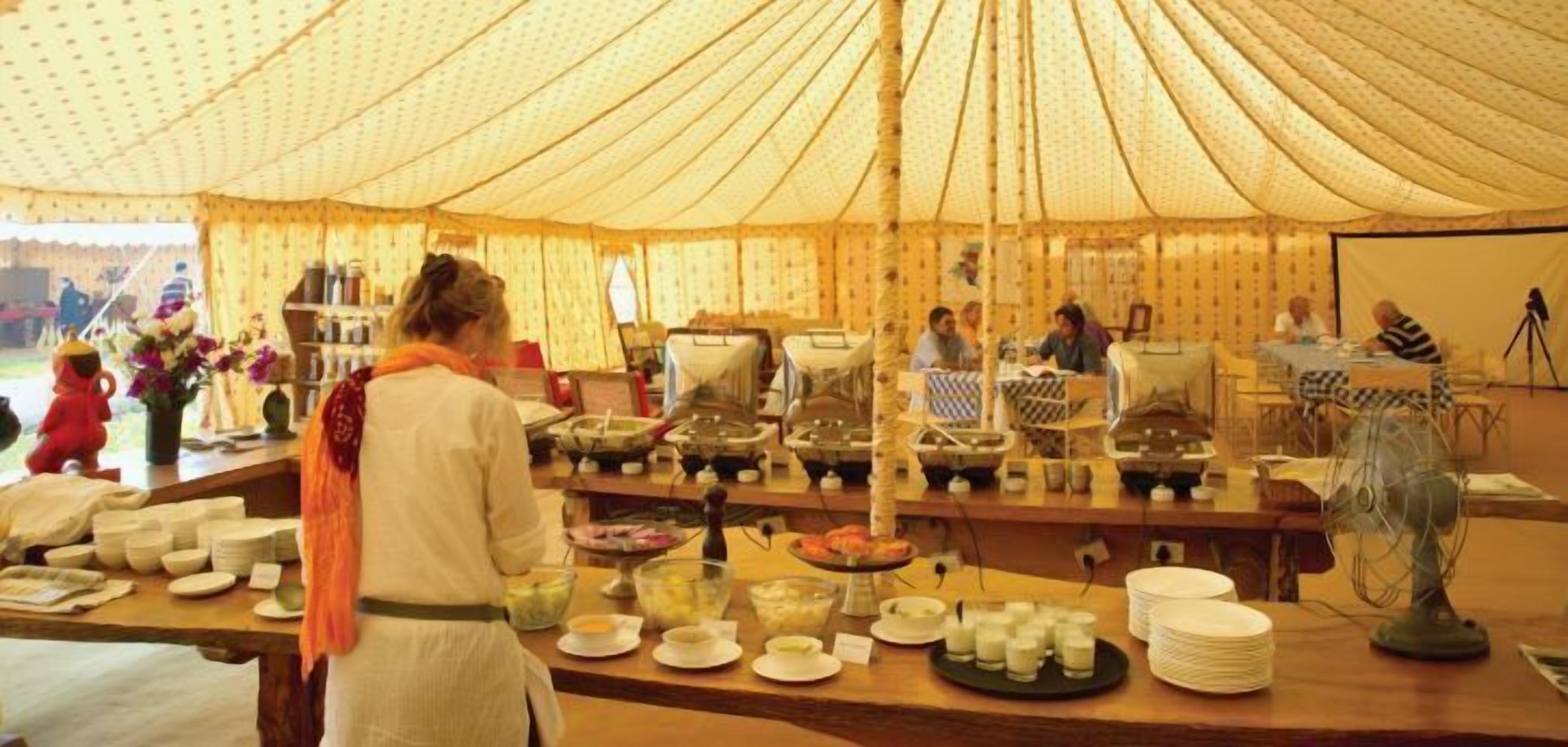 Un buffet installé dans un espace sous tente, avec différents stands de nourriture et un ventilateur pour assurer la fraîcheur.