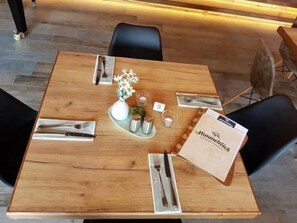A wooden dining table with a white vase of flowers, a menu, and cutlery. - Hotel Reich an der Rems (Schorndorf)