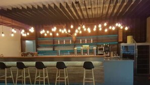 A bar area with wooden bar stools, a counter with bottles, and hanging pendant lights. - Hotel Reich an der Rems (Schorndorf)