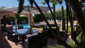 Ein Poolbereich im Freien mit Liegestühlen, einem Tisch und Sonnenschirmen.