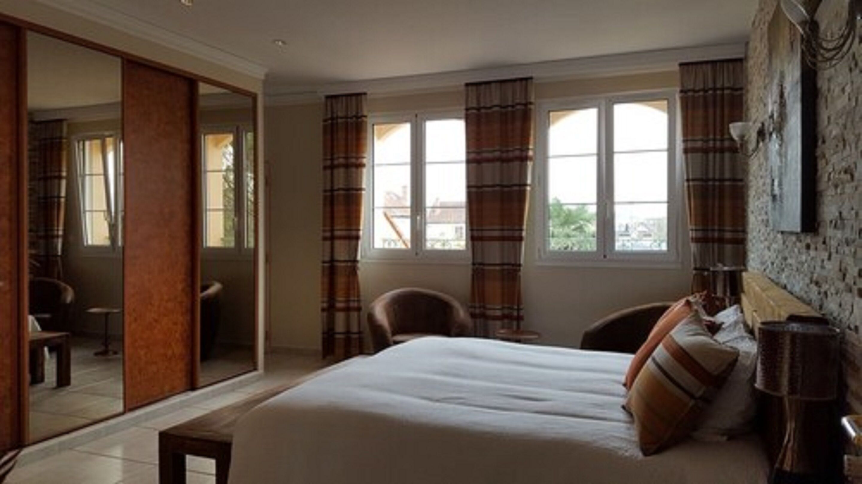 Quarto com uma cama grande, uma cadeira, uma escrivaninha e vista para o exterior pelas janelas.