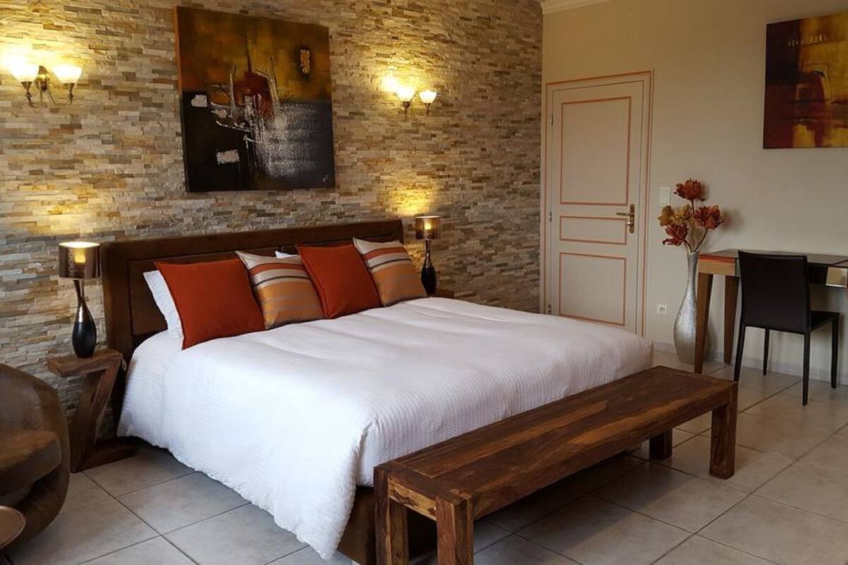 Une chambre à coucher avec un grand lit, deux lampes de chevet, un banc en bois, un bureau et une chaise.