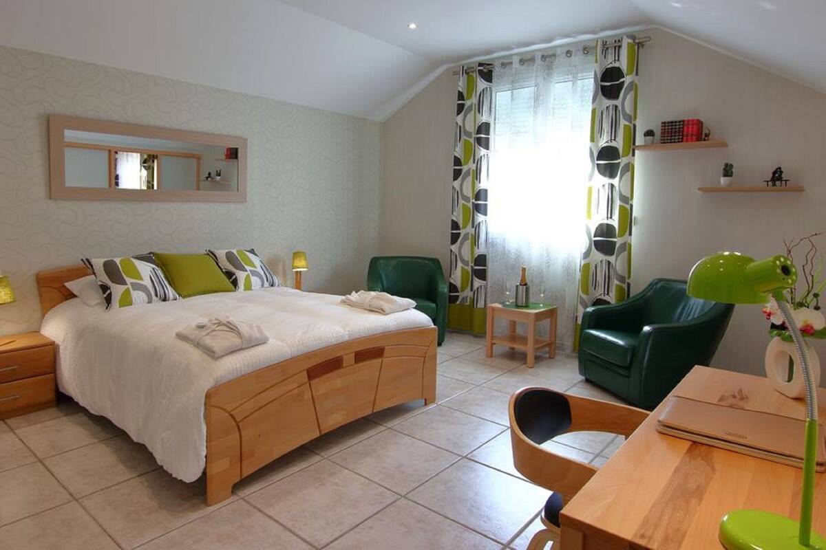 Une chambre à coucher comprenant un lit, des tables de chevet, un bureau, une chaise, un miroir et une fenêtre avec des rideaux.