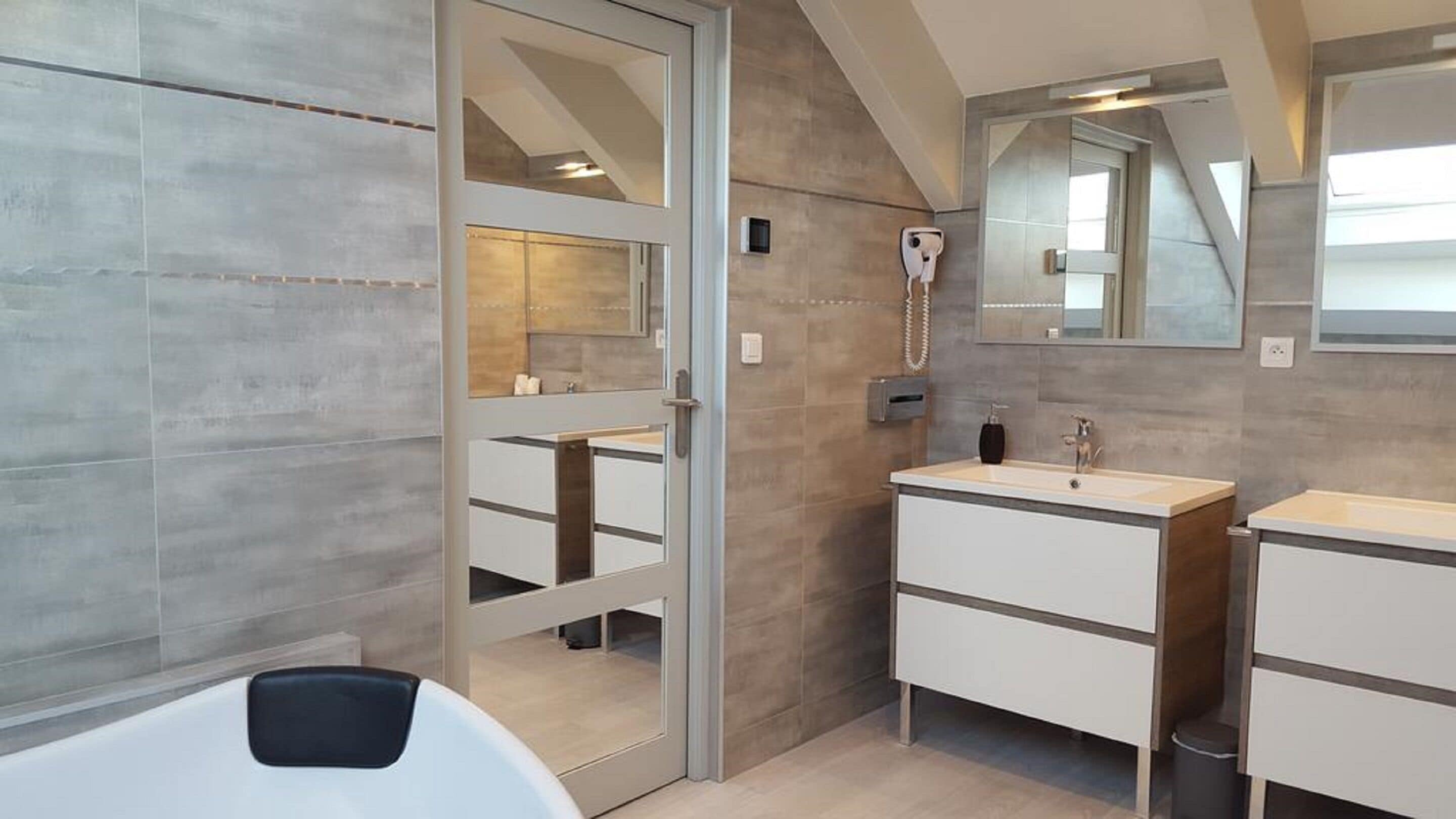 A modern bathroom with a large mirror, two sinks, and a shower area.