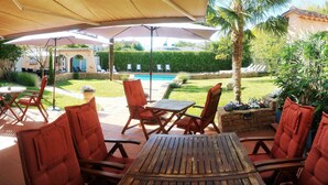 Eine Außenpatio mit Holzmöbeln und Sonnenschirmen, ein Schwimmbecken und ein gepflegter Garten.