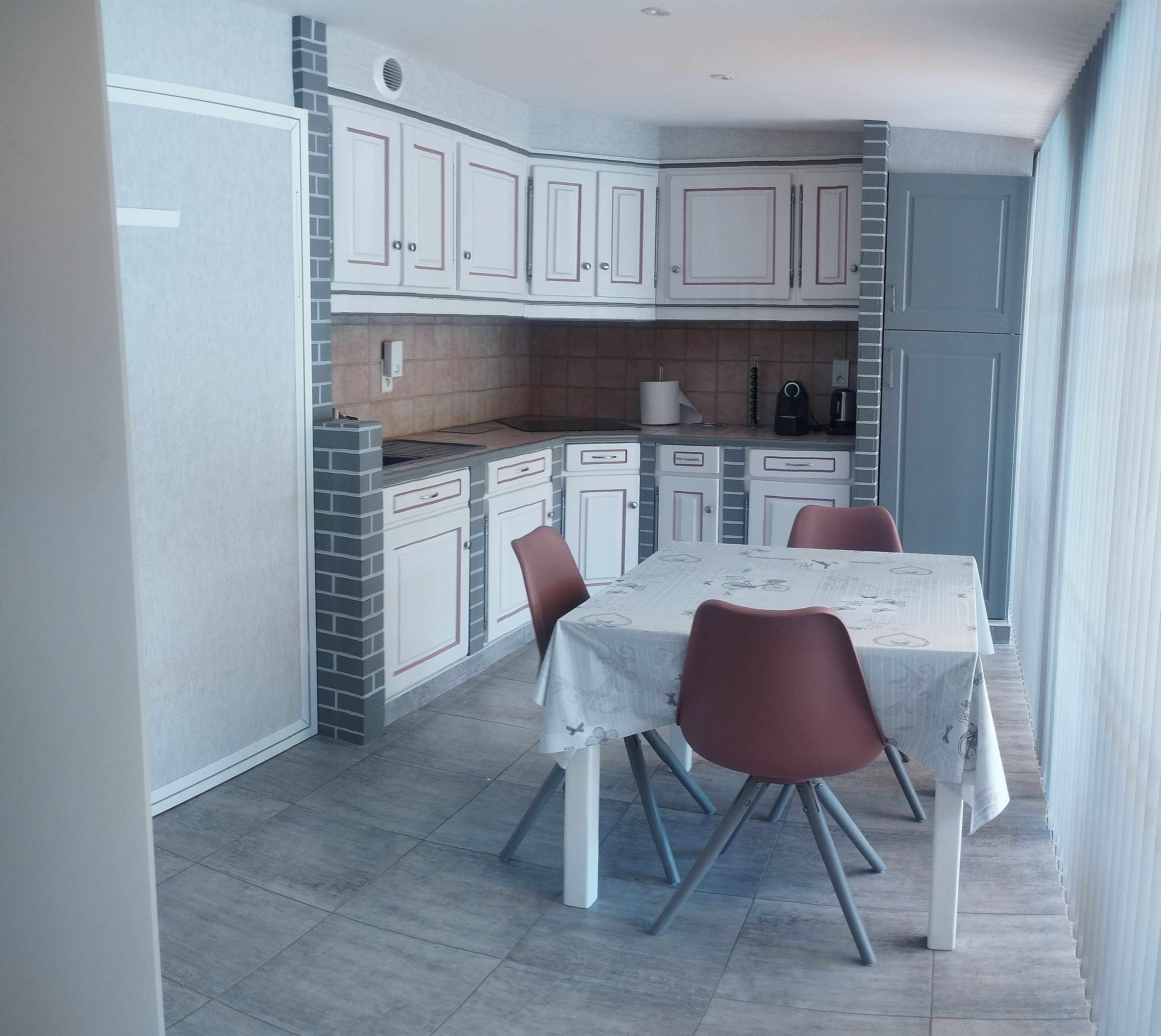 A modern kitchen with white cabinets, a brick accent wall, and a dining area with a table and chairs.