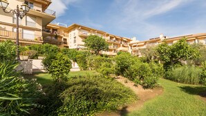A multi-story residential building with balconies, a garden area with various plants, and a clear sky. - Résidence Pierre & Vacances Baie de Saint-Tropez - Eden Parc (Saint-Tropez)