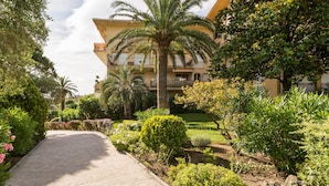 A paved pathway leading to a building with balconies, surrounded by lush greenery and palm trees. - Résidence Pierre & Vacances Baie de Saint-Tropez - Eden Parc (Saint-Tropez)
