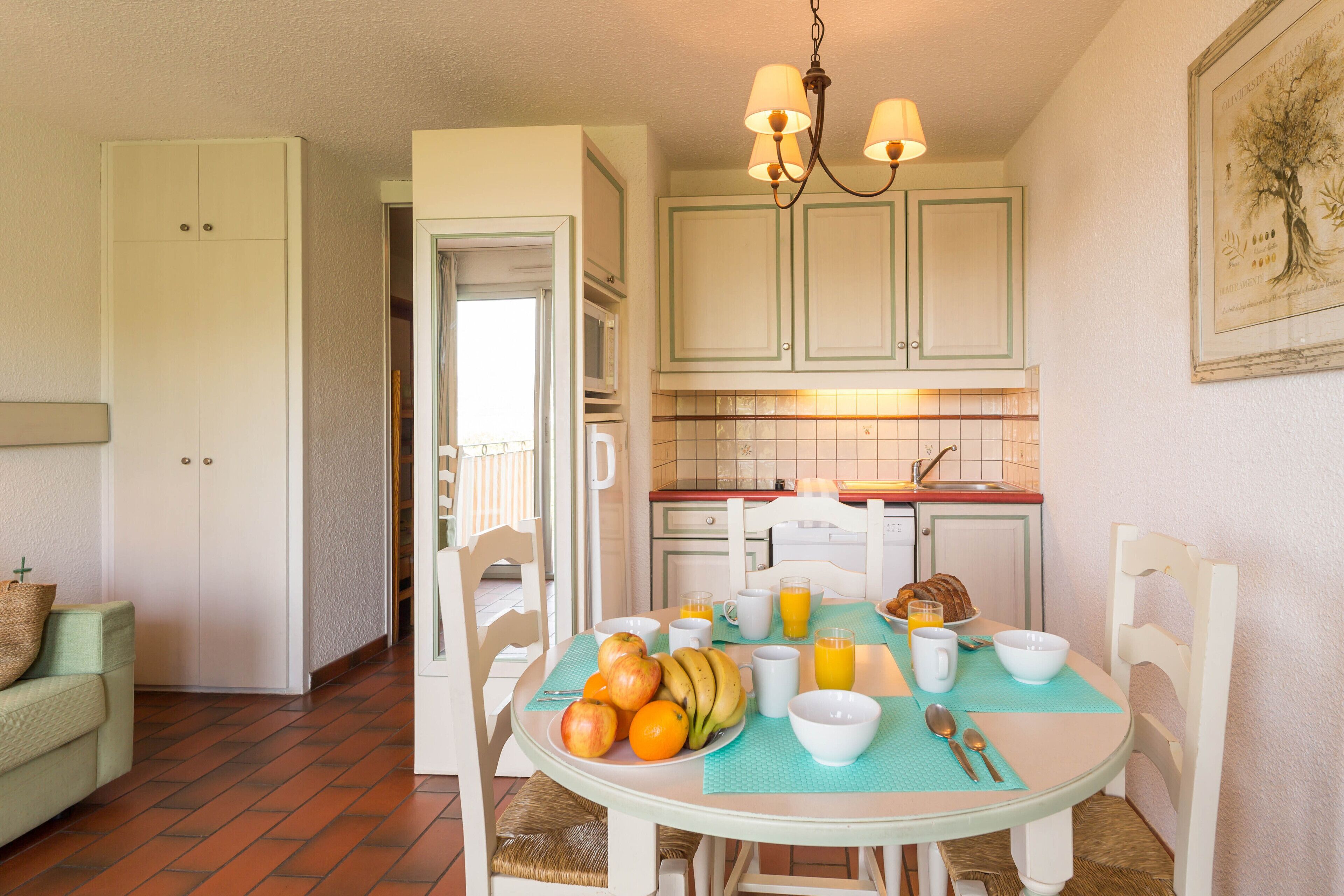 A dining area with a table set for breakfast, including fruits, a loaf of bread, and a cup of coffee.