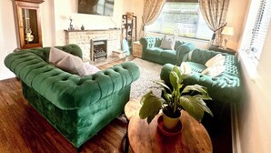 Una sala de estar con sofás verdes, una chimenea, un reloj y una araña.