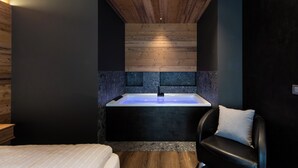Een moderne badkamer met een houten plafond, een zwart bad en een zwarte stoel met een kussen.