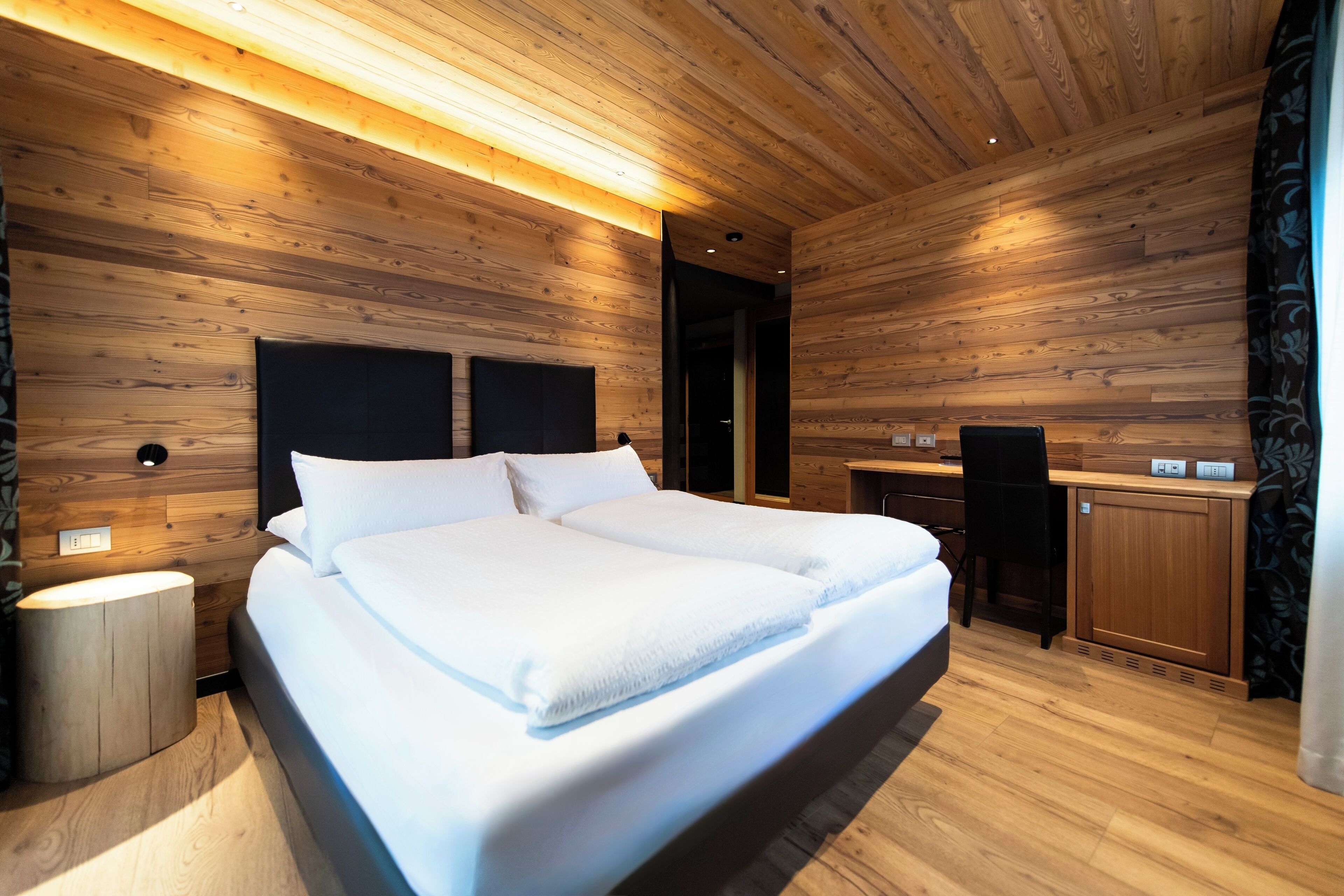 A modern bedroom with a wooden ceiling, a large bed, a bedside table, and a desk with a chair.