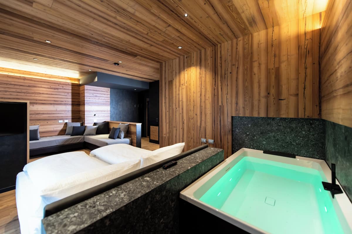 A modern hotel room with wooden panel walls, a large bathtub, and two beds with white linens.