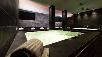 A modern spa with a large hot tub, dark stone walls, and a minimalist design.