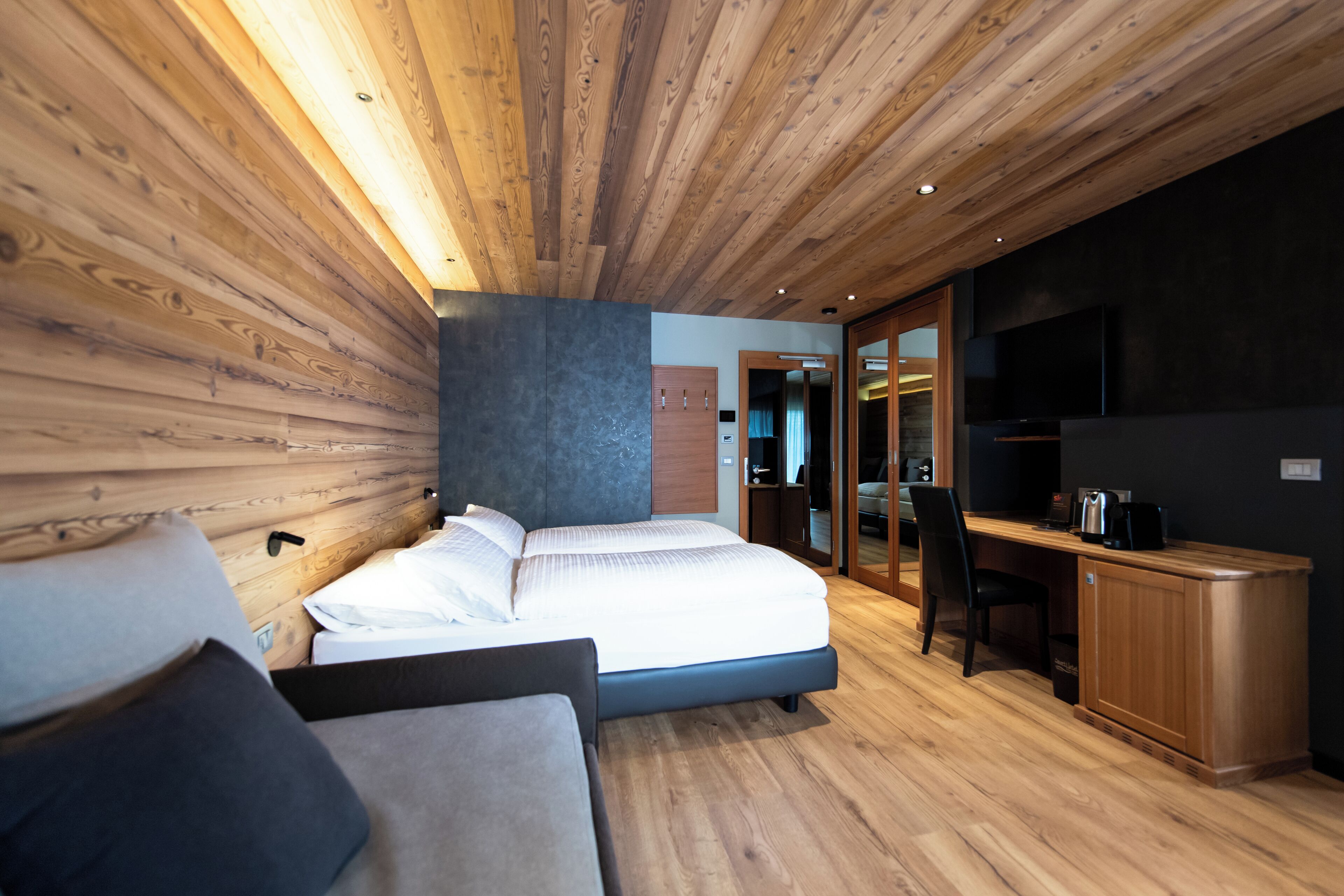 A modern bedroom with a wooden ceiling, a large bed, a desk, and a TV.