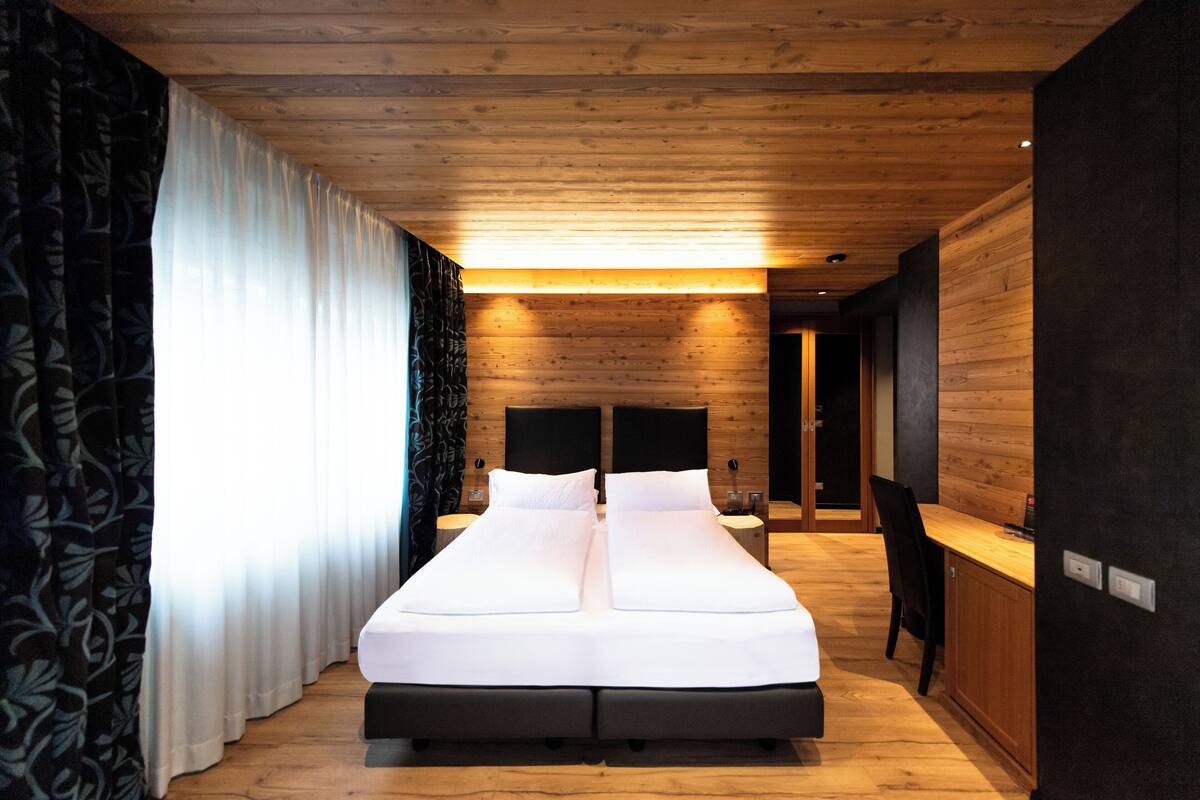 A modern bedroom with a wooden ceiling, a large bed, a desk, and a chair.