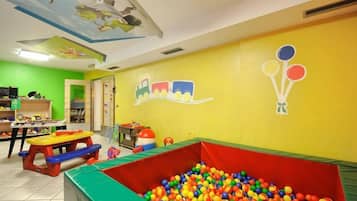 Espaço infantil com piscina de bolinhas, brinquedos coloridos e um mural de um trem e balões na parede.
