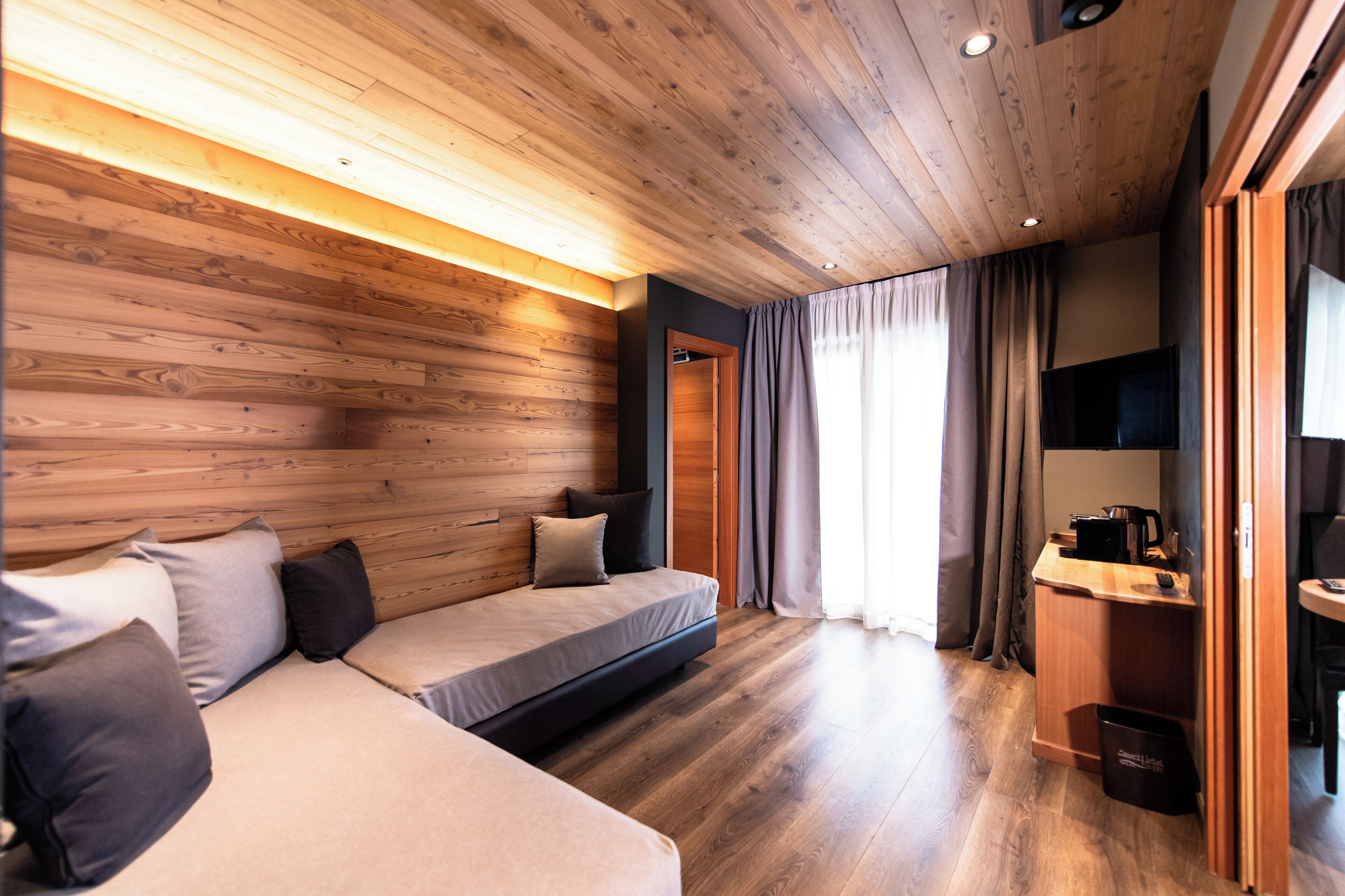A modern room with wooden walls, a sofa, a bed, a desk, and a TV.
