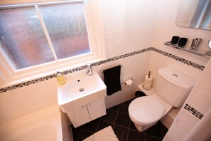 A bathroom with a white sink, toilet, and bathtub. There is a window above the sink and a mirror above the toilet. - Abbey Court (Sherborne)