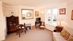 A living room with a fireplace, a television, a sofa, and a window with a view of the outside. - Abbey Court (Sherborne)