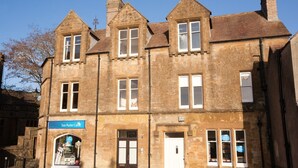 A historic stone building with multiple windows, a sign for 'Sue Ryder Care', and a small shop window. - Abbey Court (Sherborne)