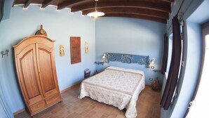 A bedroom with a wooden wardrobe, a bed with a patterned bedspread, a blue headboard, and a tiled floor. - B&B Giuggiolando (L'Aquila)