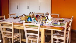 A dining table set with various food containers, a teapot, and a pitcher, surrounded by wooden chairs with woven seats. - B&B Giuggiolando (L'Aquila)