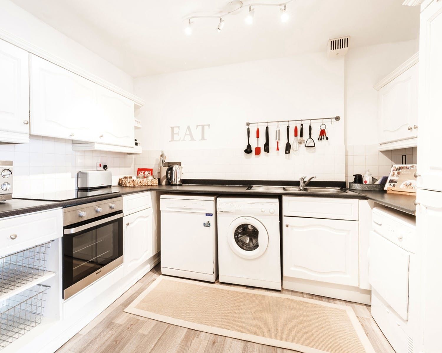 A modern kitchen with white cabinets, a built-in oven, a washing machine, and a sink.