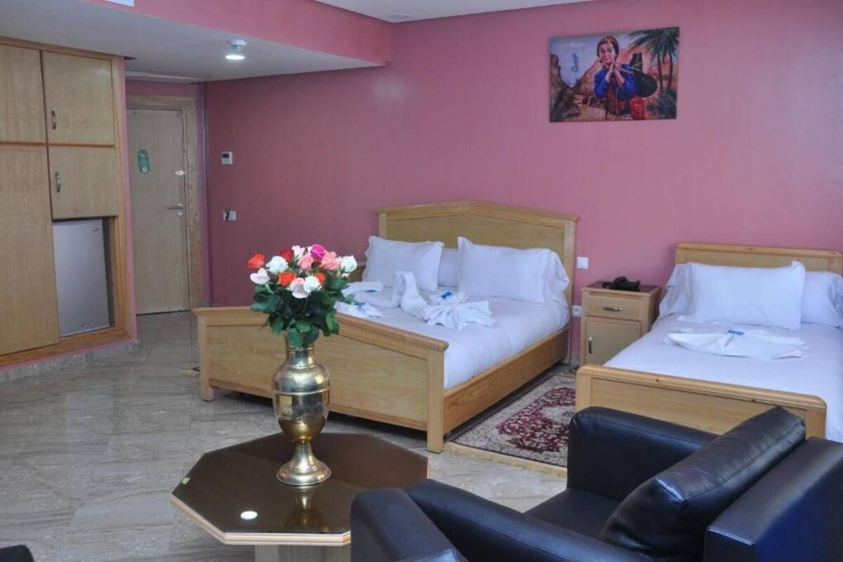 A hotel room with two beds, a wooden headboard, a nightstand, a bedside table, and a vase with flowers.