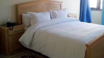 A single bed with a wooden headboard, a bedside table with a lamp, and a patterned rug on a tiled floor.