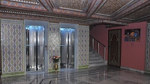 Un hall d’entrée aux murs recouverts de carreaux décoratifs, doté d’un sol en marbre et d’un escalier avec une rampe en métal.