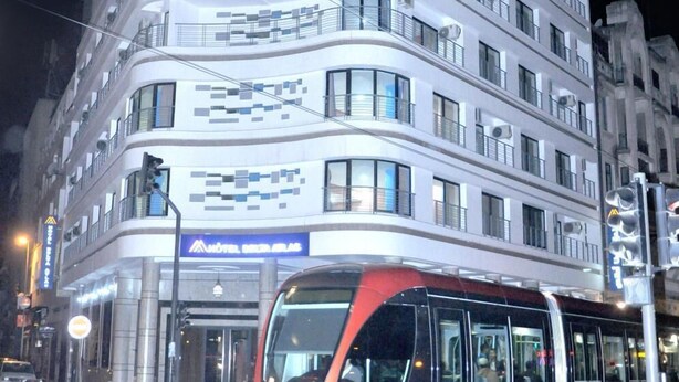 Un hôtel moderne à la façade incurvée, doté de nombreux balcons et d’une enseigne bien visible indiquant « HÔTEL DELTA ATLAS ».