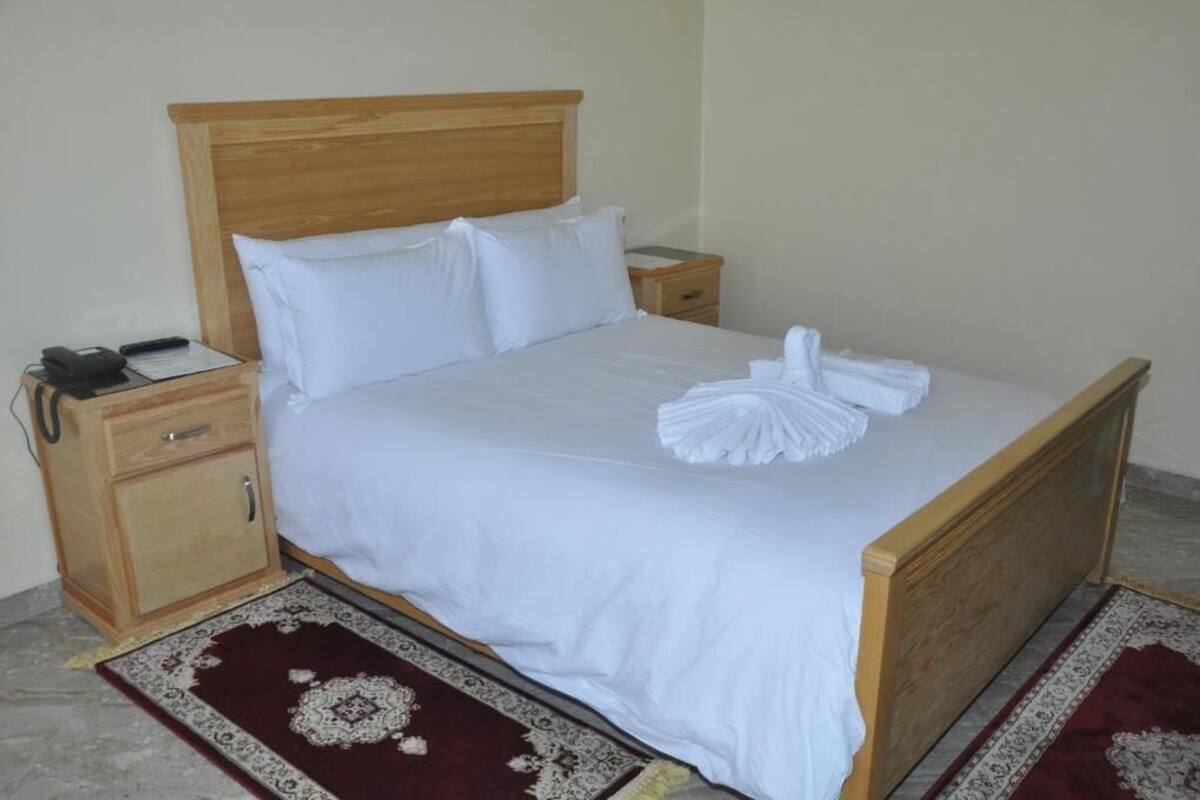 A neatly made bed with white linens, a wooden headboard, and a matching wooden nightstand with a phone and a notepad.