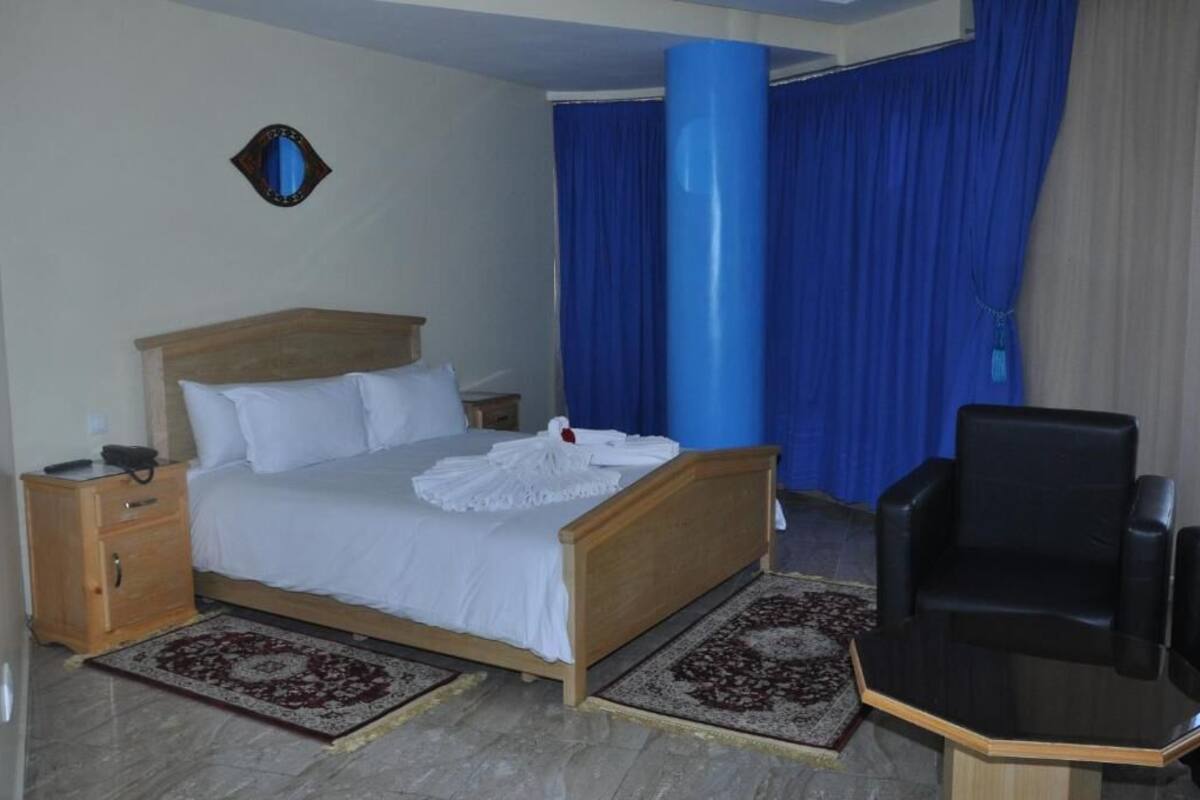 A hotel room with a wooden bed, a nightstand, a black leather chair, and a blue curtain.