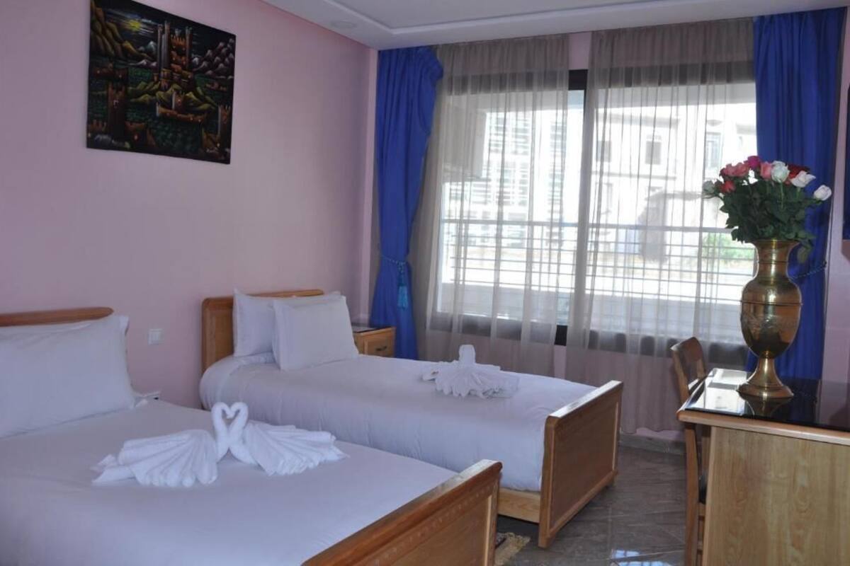 A hotel room with two beds, a desk, and a window with curtains.