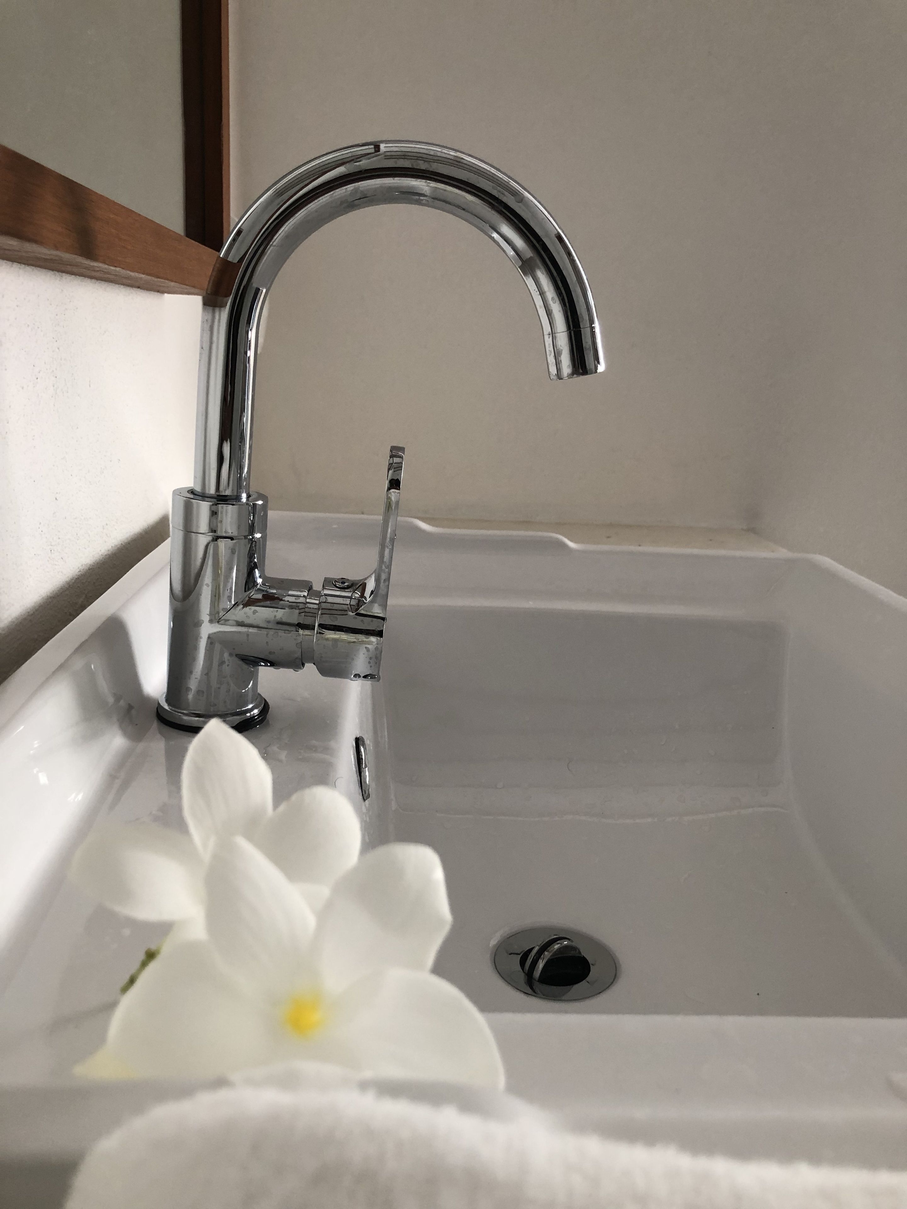 A bathroom sink with a chrome faucet, a white flower, and a towel.