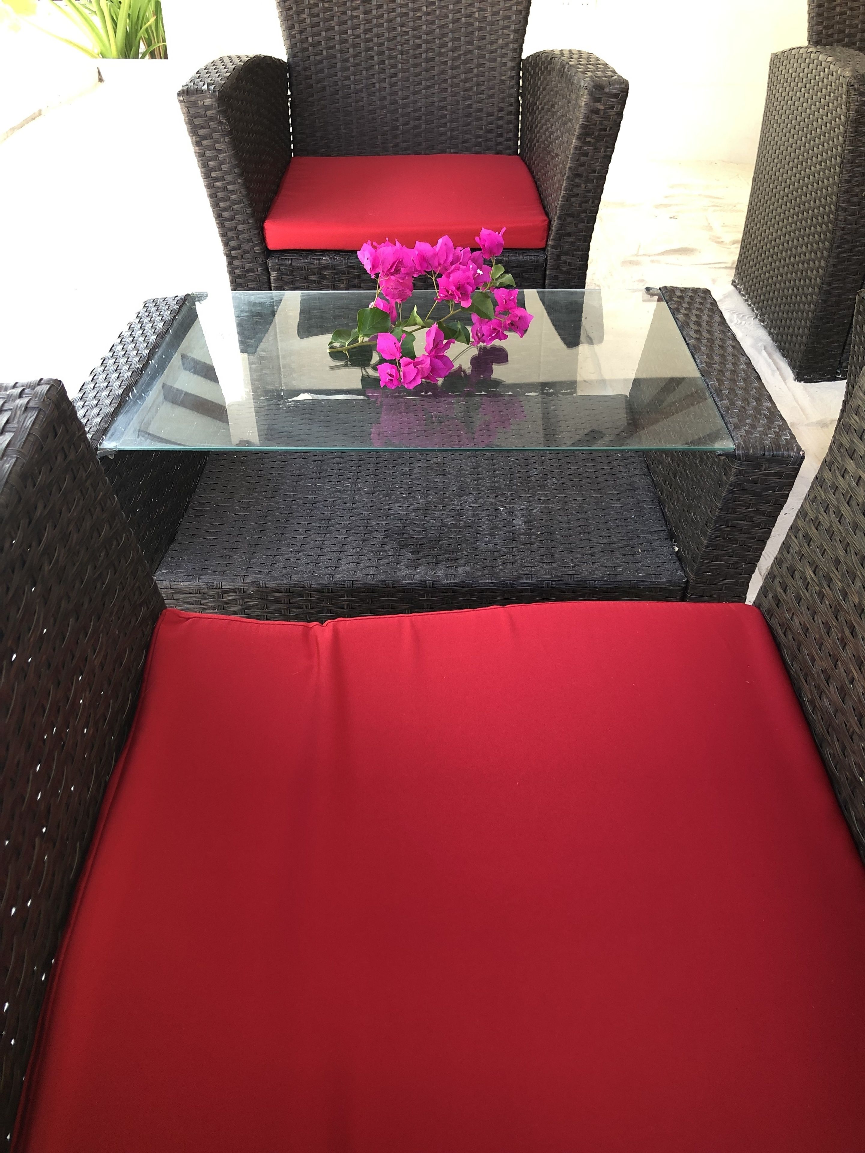 A wicker chair with a red cushion and a glass-top table with a bouquet of pink flowers.